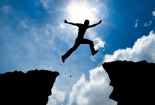 Silhouette of a person leaping between two cliffs against a background of a blue sky